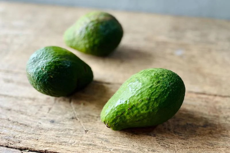 Group of three Semil 34 avocados with rough, dark green skin on a rustic wooden table.