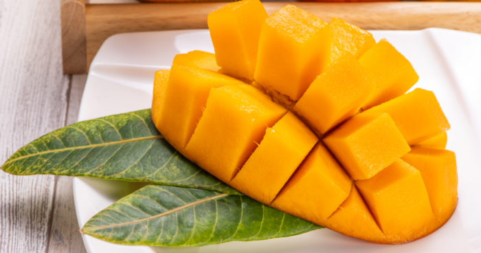 Freshly cut cubes of Mango Osteen on a plate with vibrant green leaves, showcasing the sweet and juicy flesh.